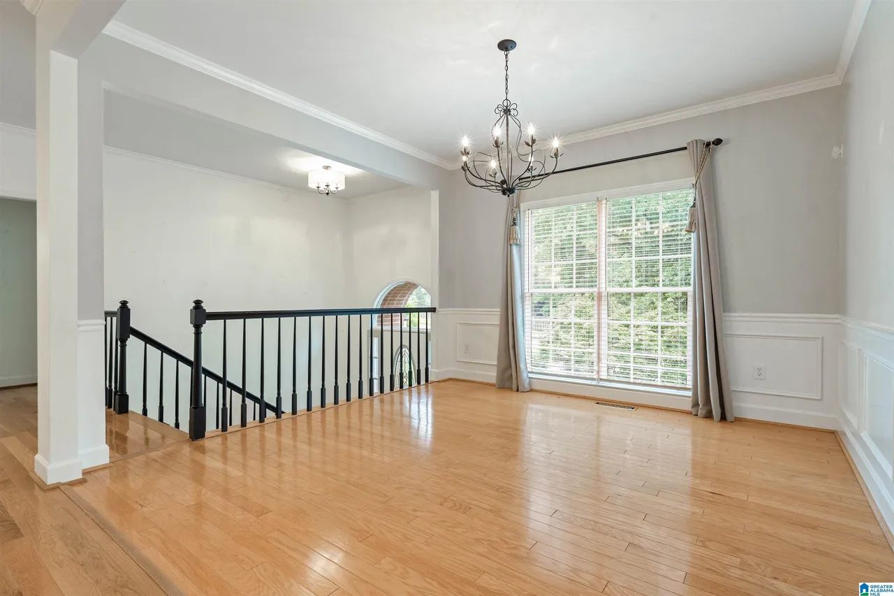 Formal dining room with wainscoting and chandelier beside the staircase